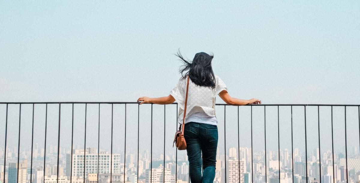 a woman standing in front of a railing looking out to a city