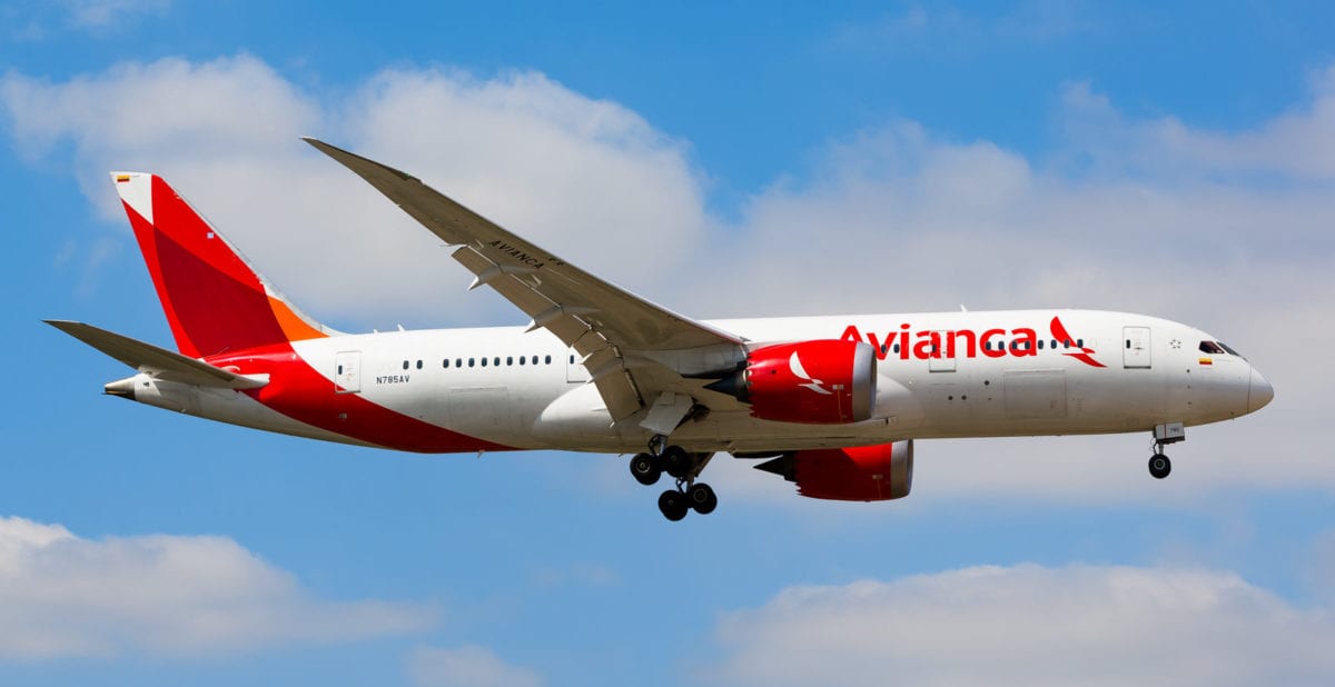 A large Avianca passenger jet flying through a cloudy blue sky