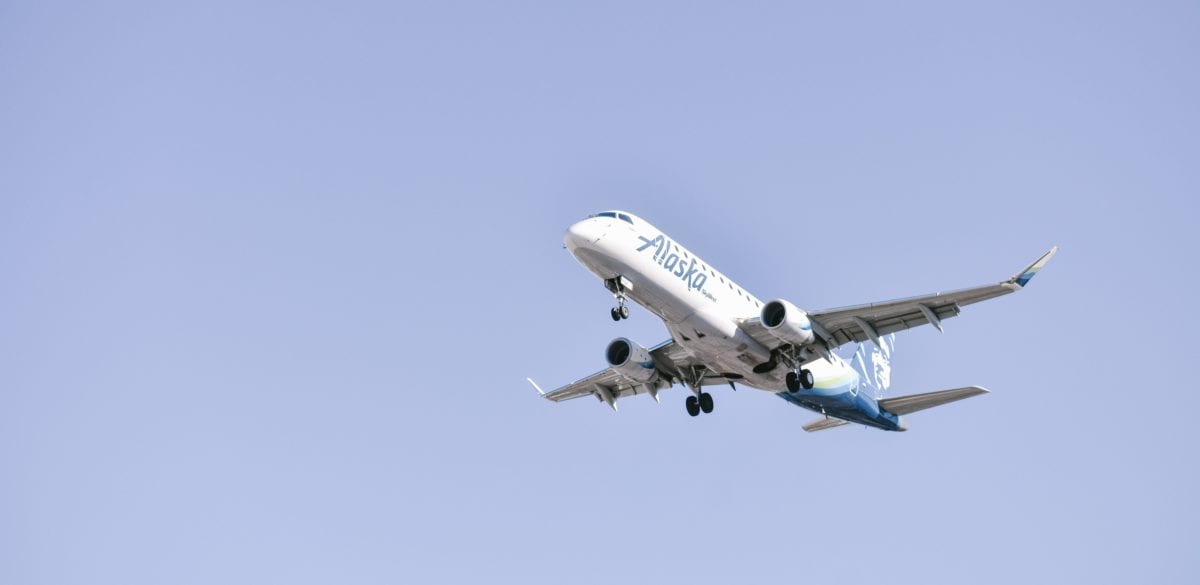 A large alaska passenger jet flying through a blue sky