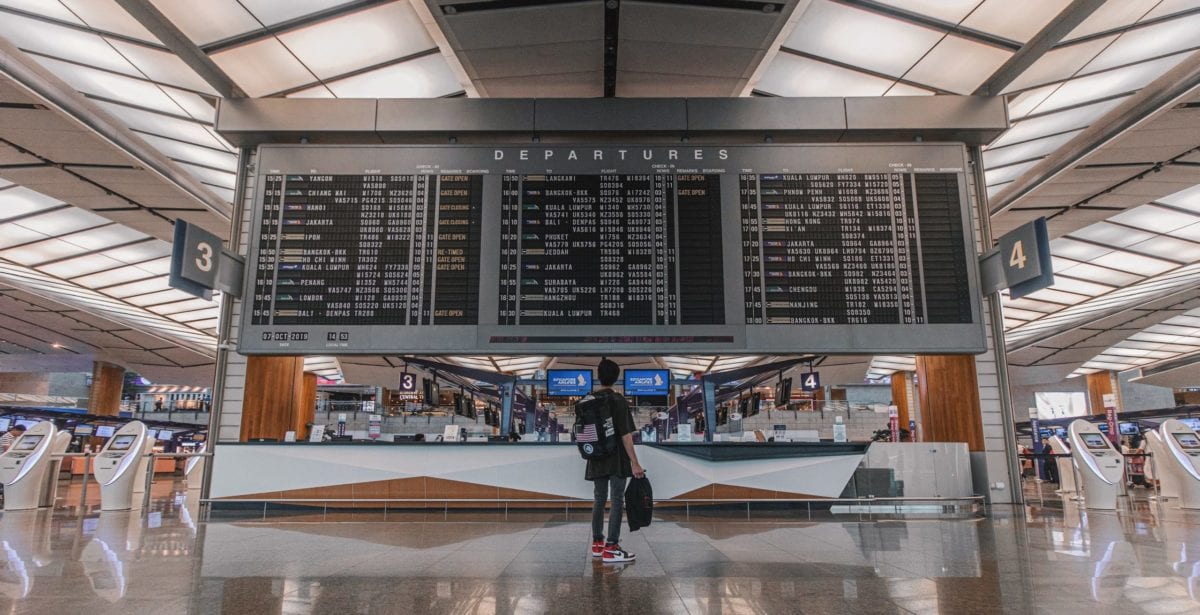 a person standing in front of an airport departures board