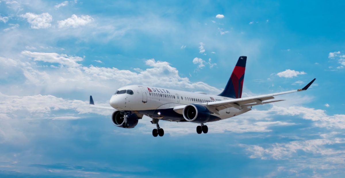 A large delta passenger jet flying through a cloudy blue sky