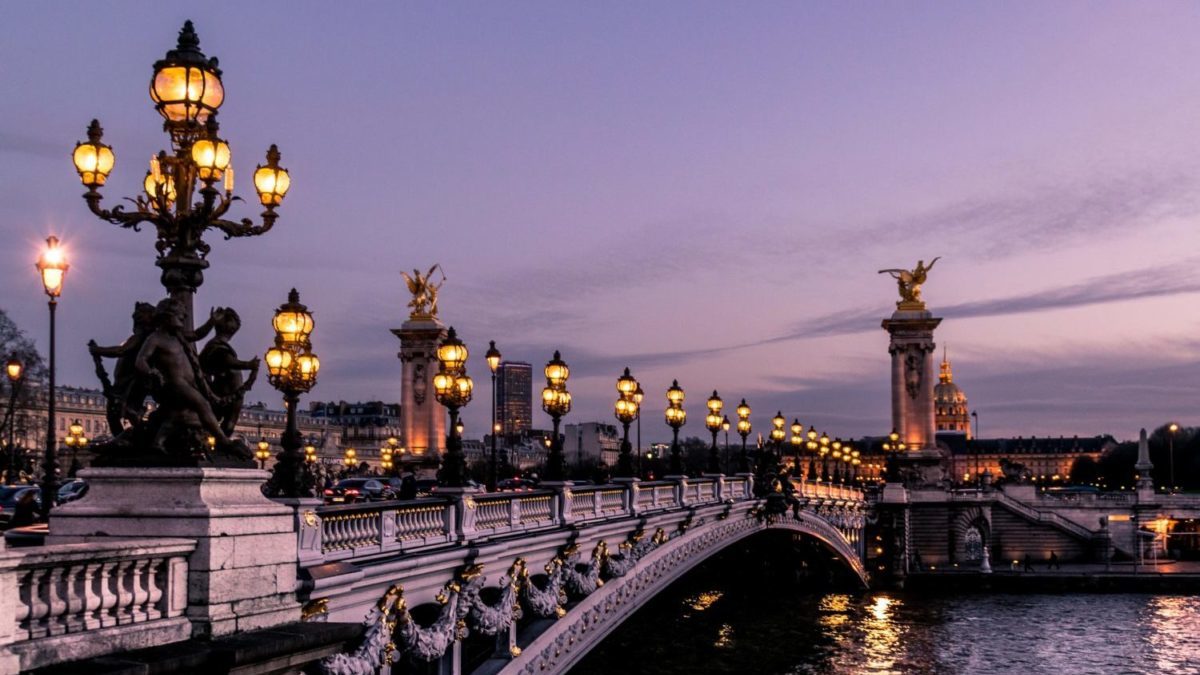 A large bridge lit up at night with Pont Alexandre III in the background