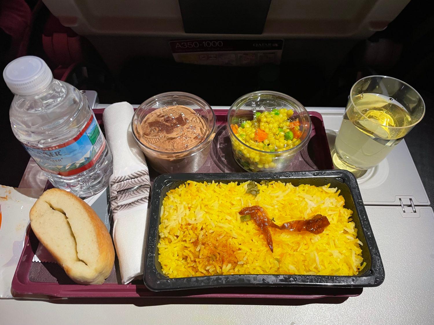 a platter with chicken and rice and sides on an airplane tray