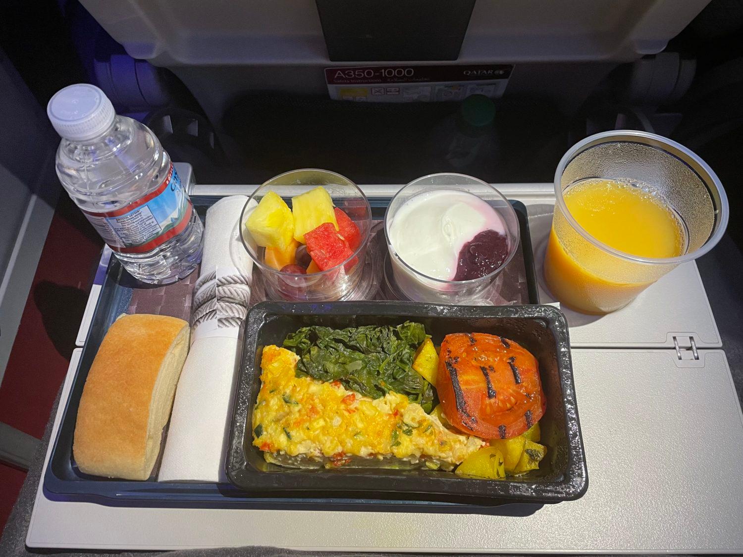 a tray of breakfast with fruit and yogurt on an airplane tray table