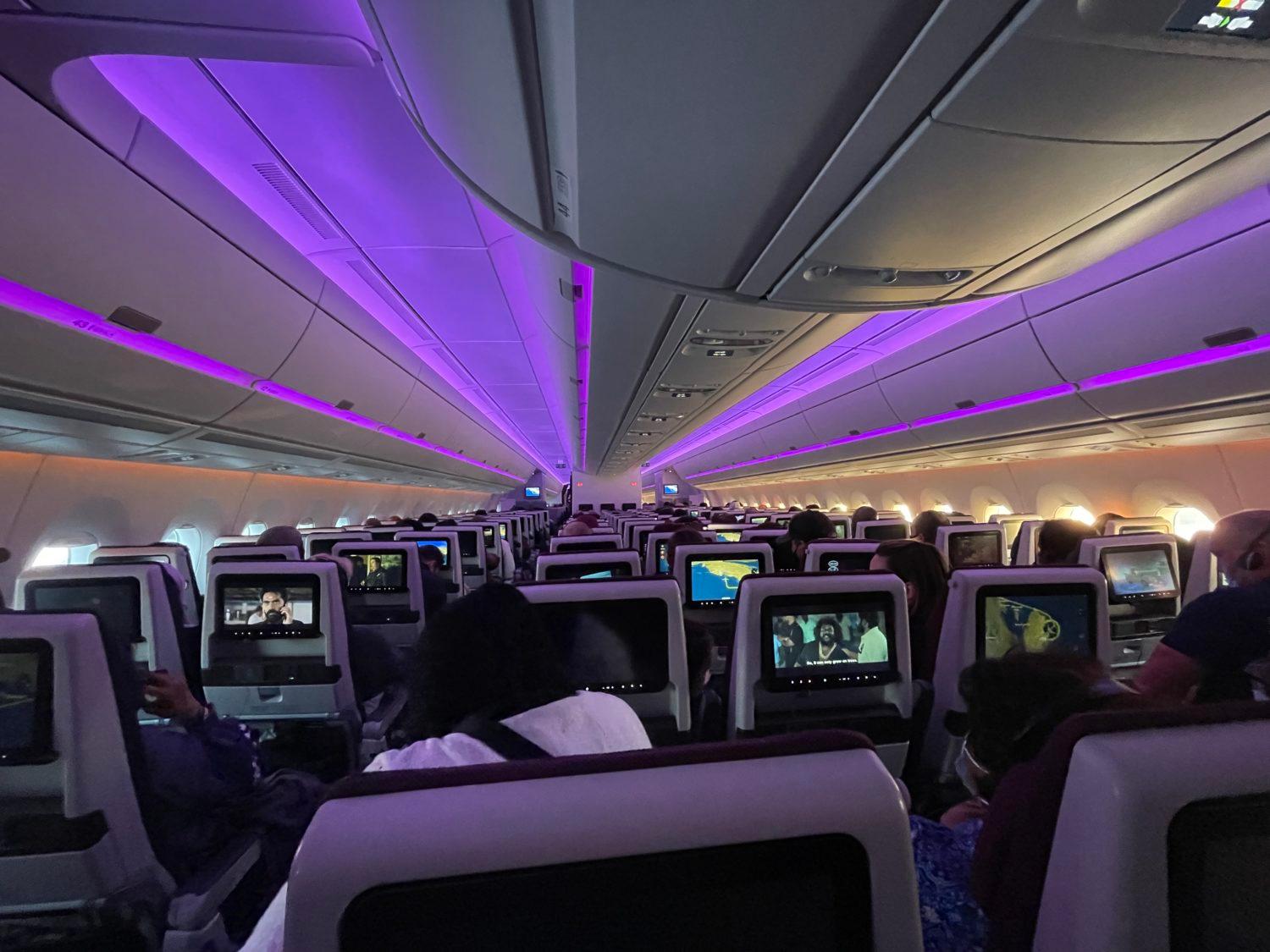 an economy cabin on a plane with purple lighting overhead