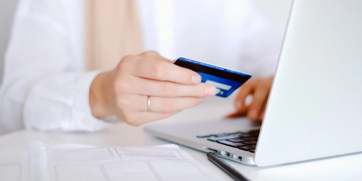 A person holding a credit card at a laptop