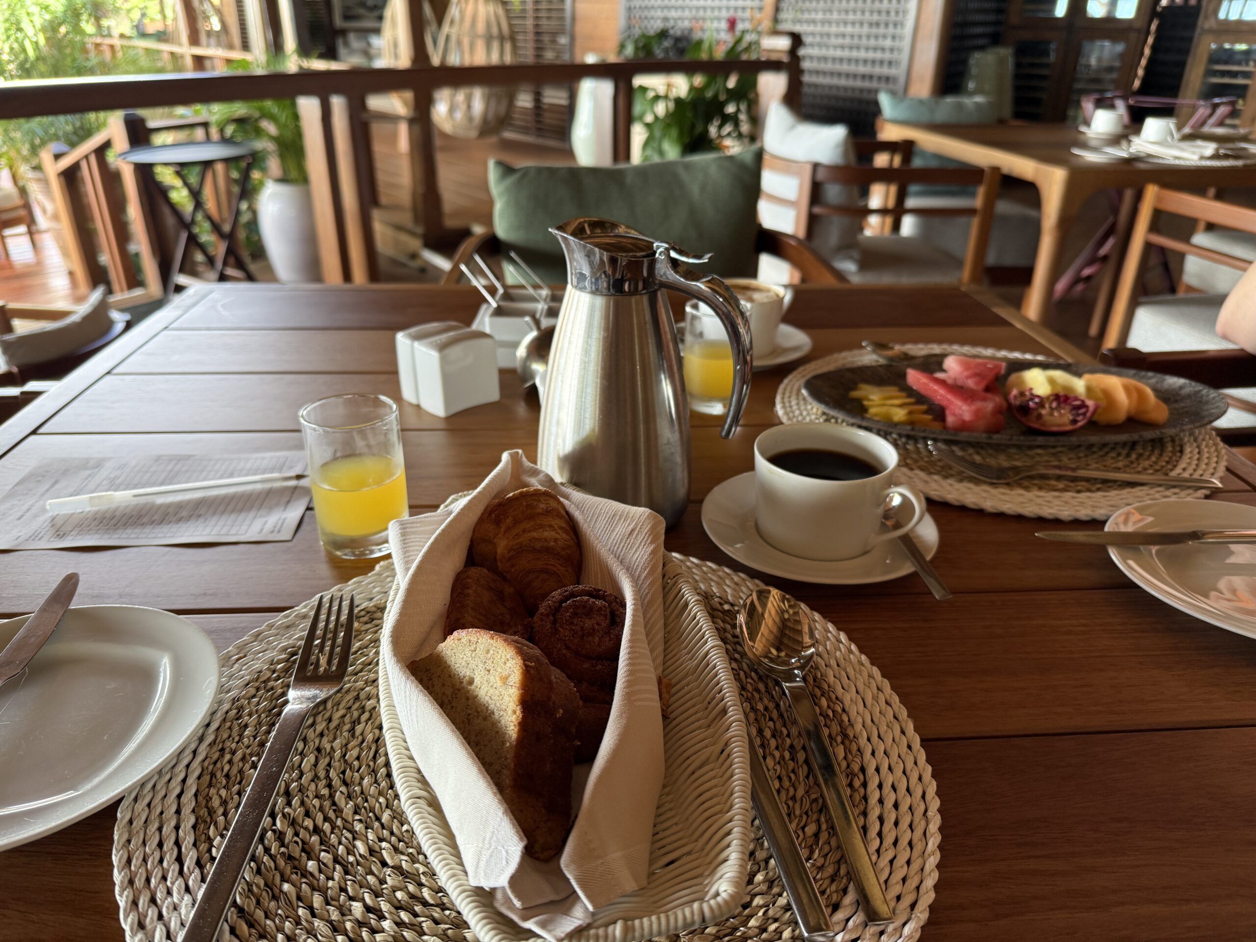 a basket of pastries and platter of fruit with coffee on the table