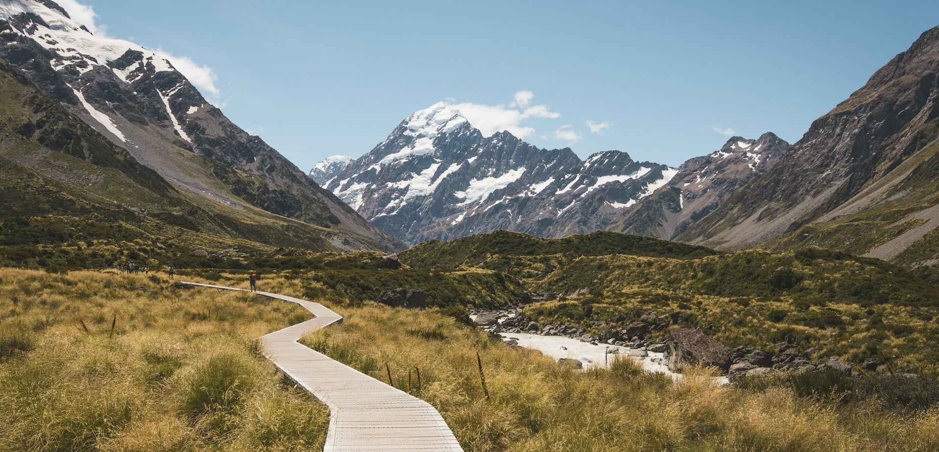 Hooker Valley Track in New Zealand showing a boardwalk in front of massive mountains on a clear day.