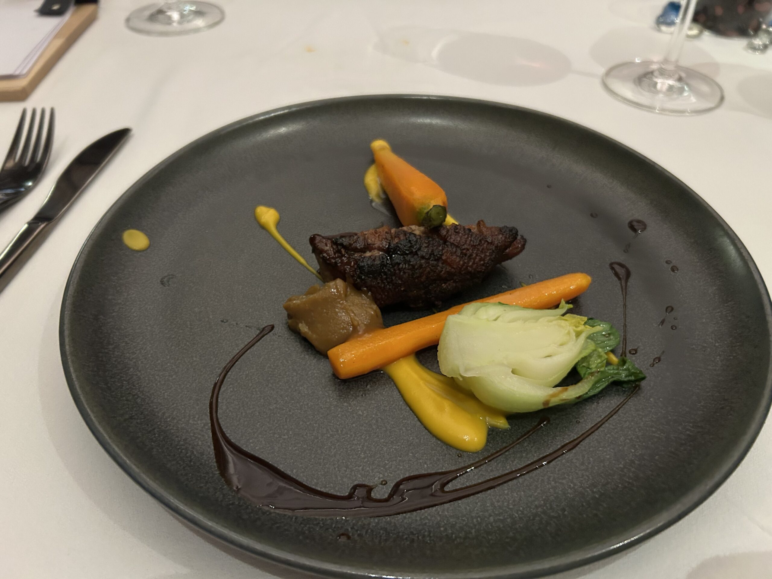 duck course with carrots and delectable sauces on a black plate 