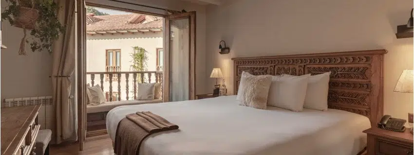 King sized bed with hand-carved heaboard and open french doors leading out to a balcony. 