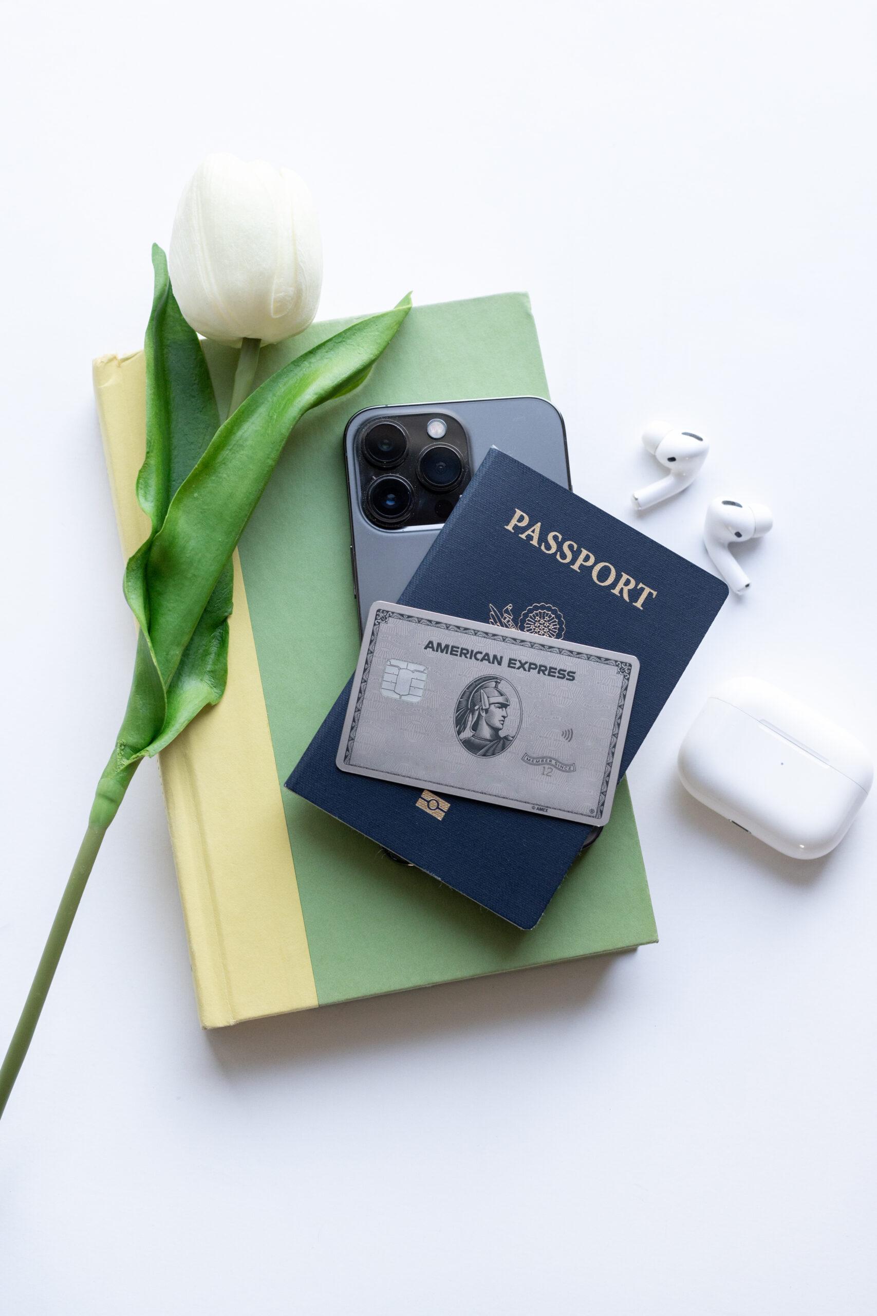 amex platinum card sitting on a passport, cell phone, and book 