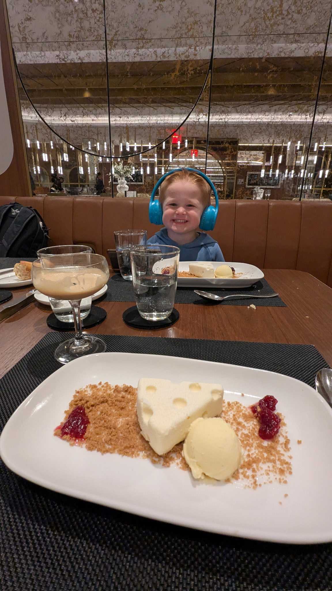 A three-year-old boy with headphones eating cheesecake in the Delta One Lounge at JFK.
