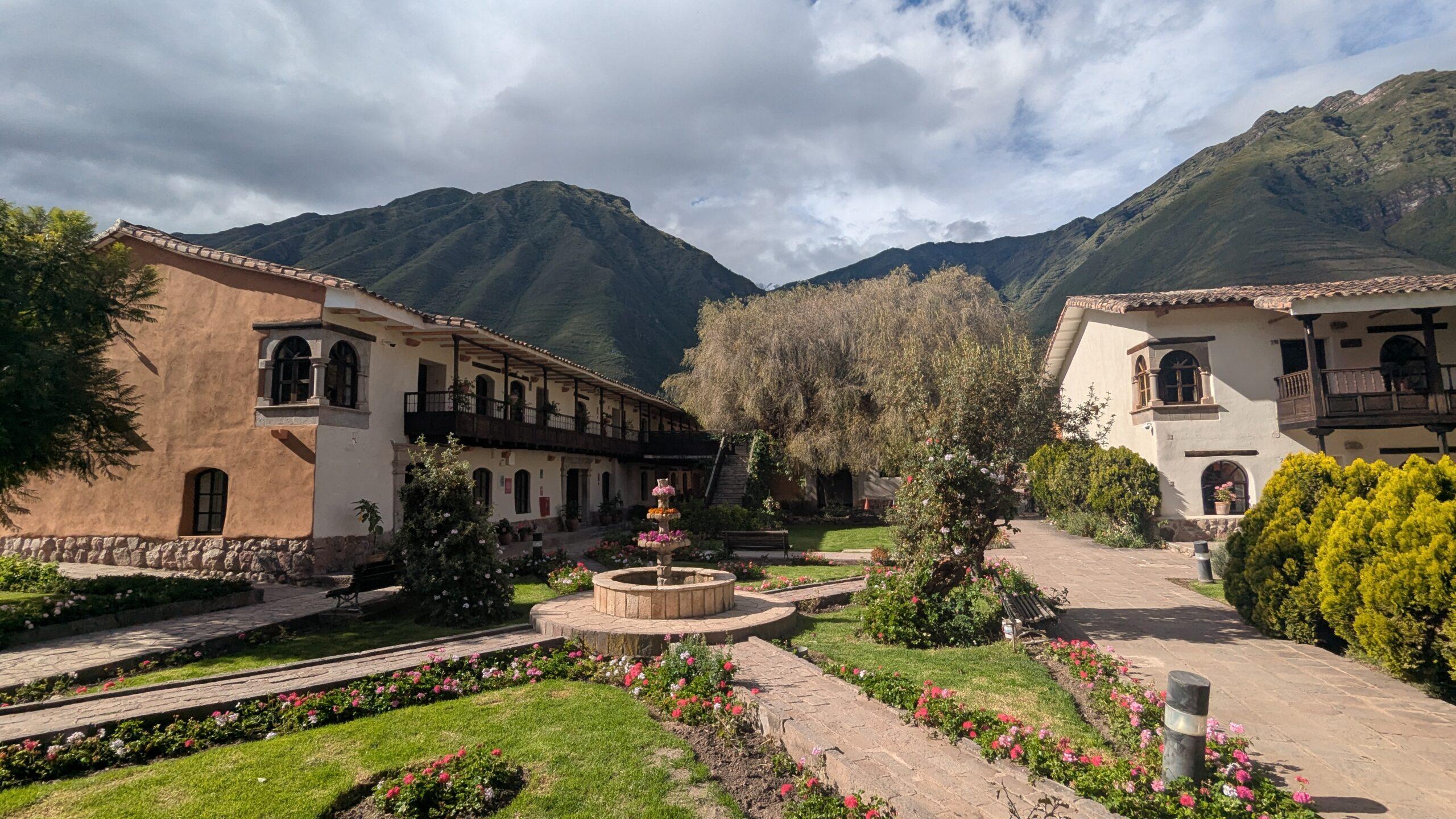 Two colonial-style buildings and flower garden at the Sonesta Yucay hotel in peru, surrounded by mountains. 