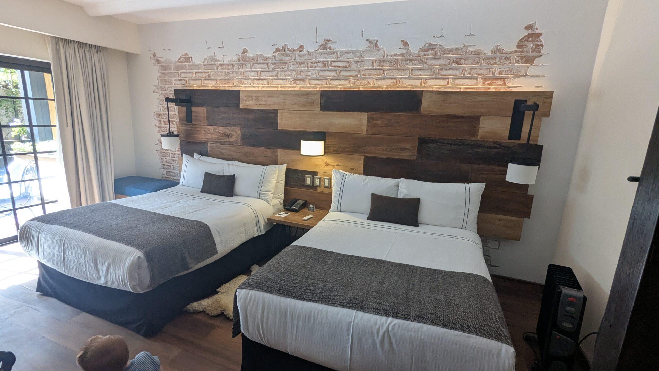 Two beds in a hotel room at Sonesta Yucay with a night stand between them and reading lamps mounted to the wall. 