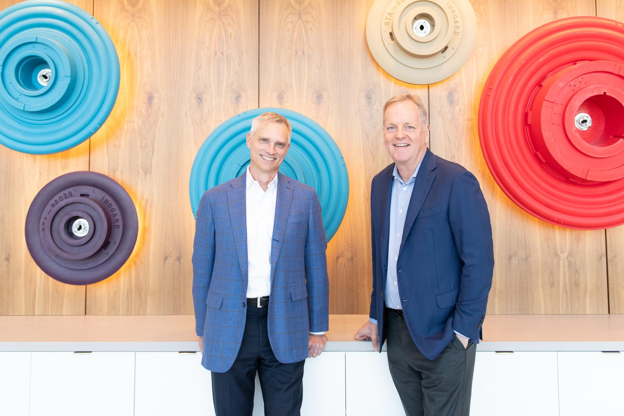 Ex-American Airlines CEO Defends Higher Fares for Solo Flyers 2 two men standing in front of a wooden wall with colorful circles
