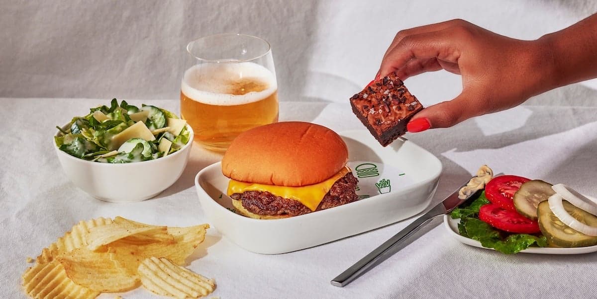 hand taking a brownie from a platter with a burger