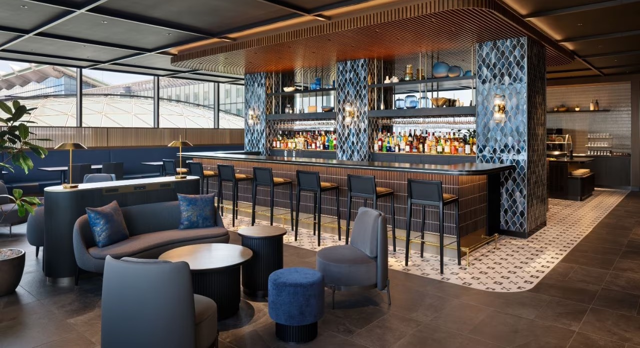 Centurion Lounge (HND) Bar Area with table seating, a fully stocked bar adorned in blue tile, and bar stools.