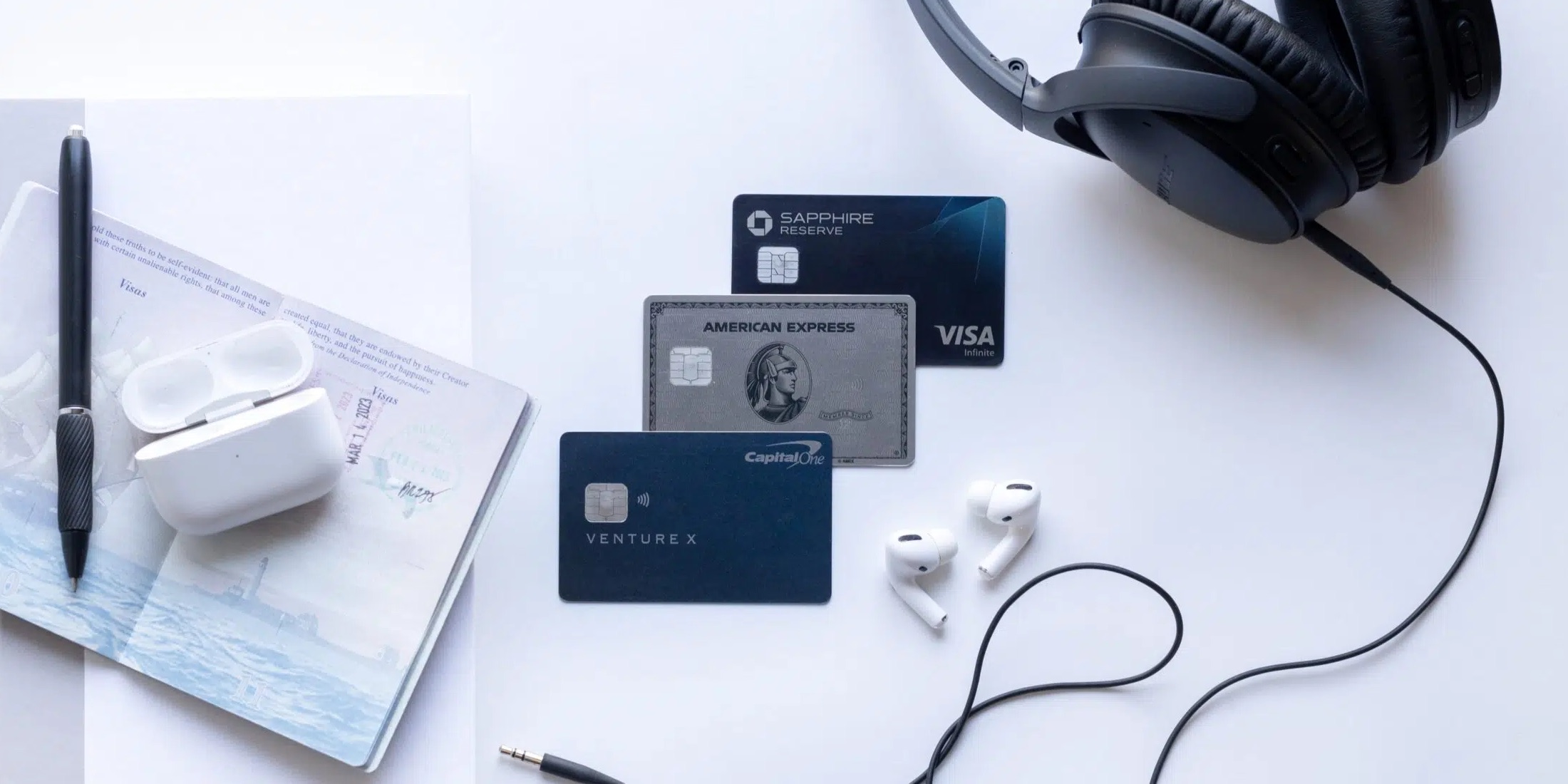Venture X, Amex Platinum, and Chase Sapphire Reserve on a white background with passport, pen, airpods and headphones. 