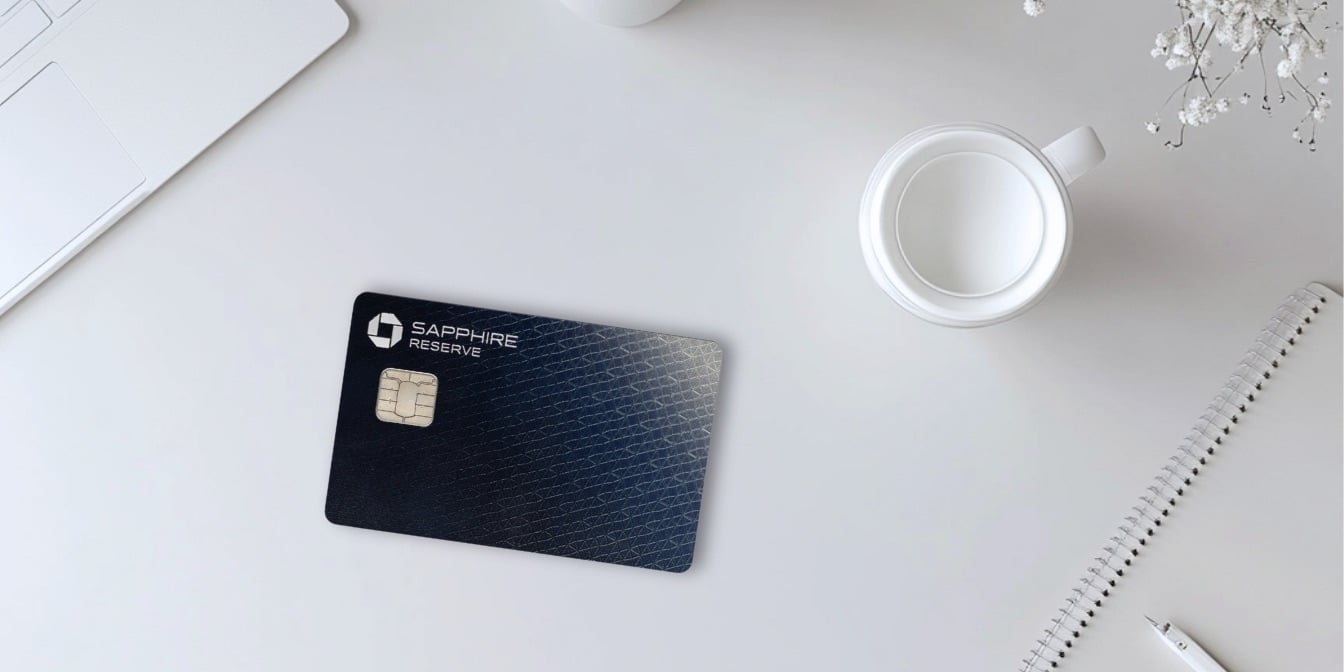 Chase Sapphire Reserve Card with a cup of coffee, notepad, pen, and laptop computer on a white background.