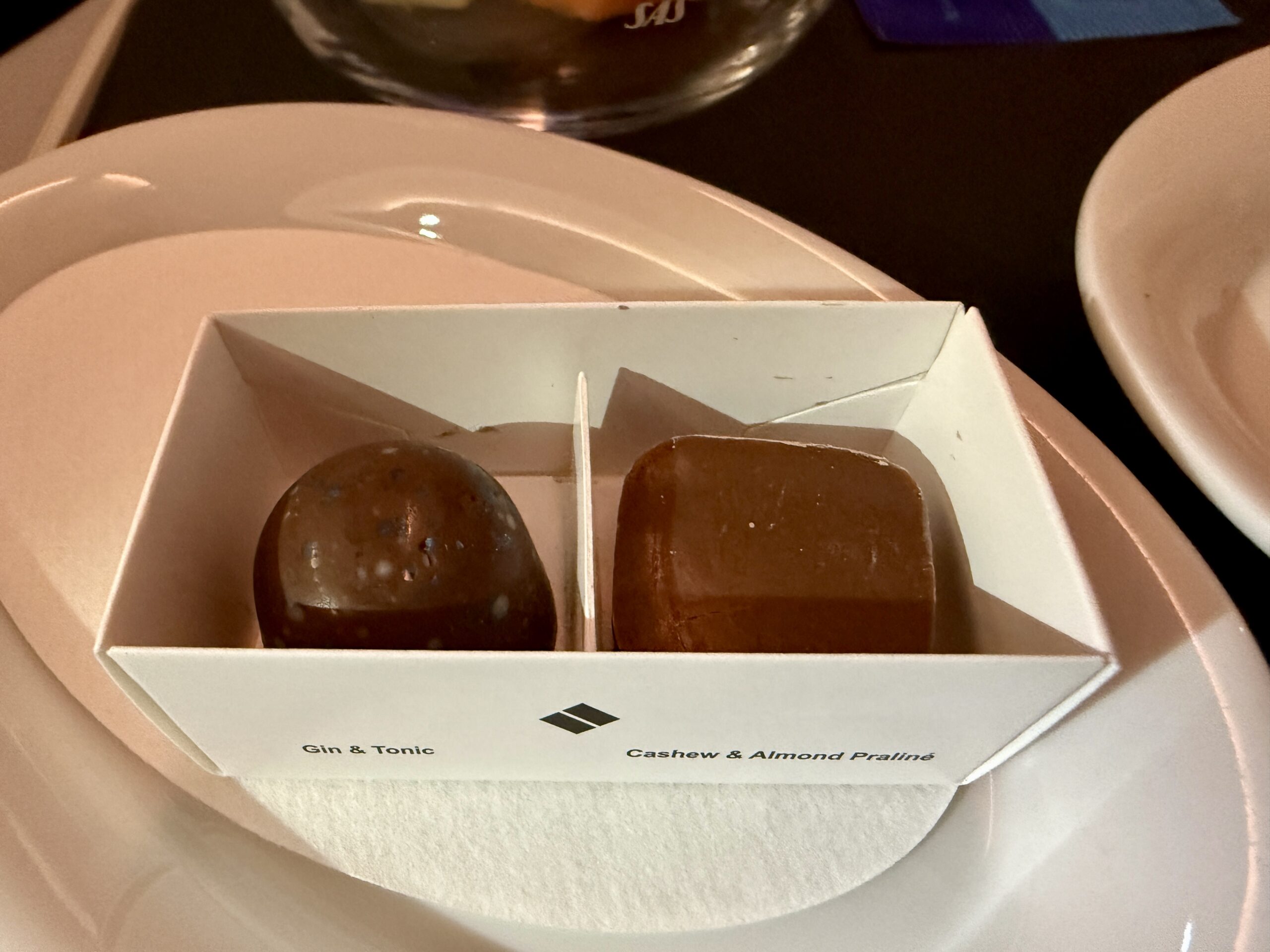 two chocolate pralines in a small white box on a plate