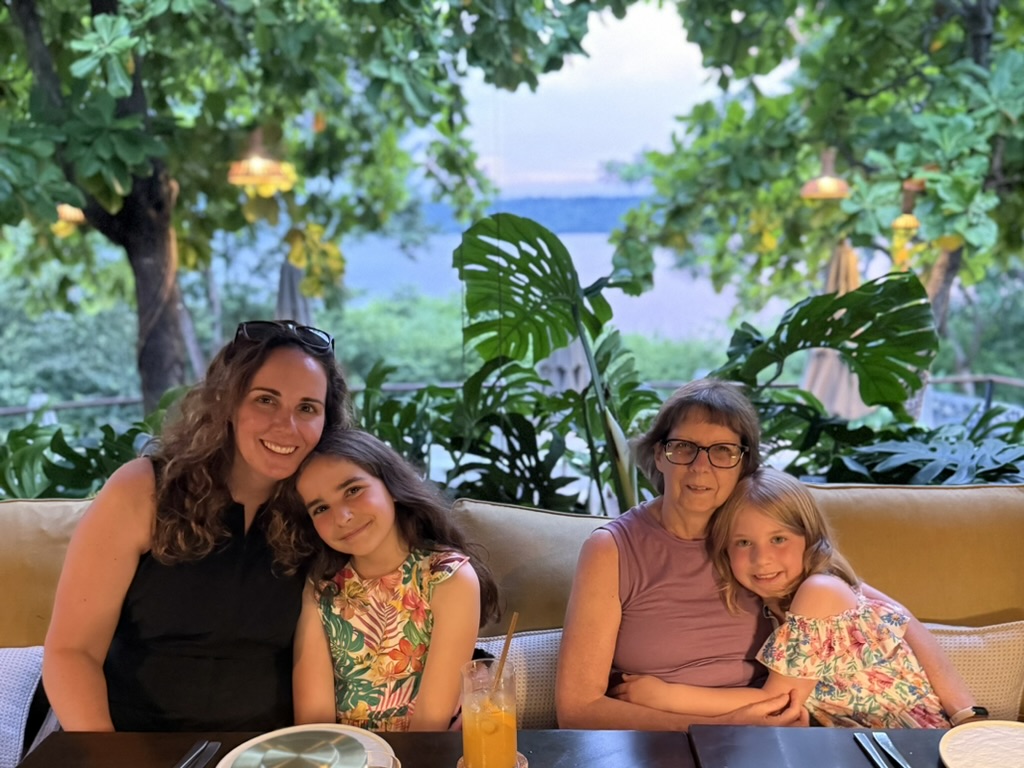 Two adult women and two young girls with trees and ocean in the background. 