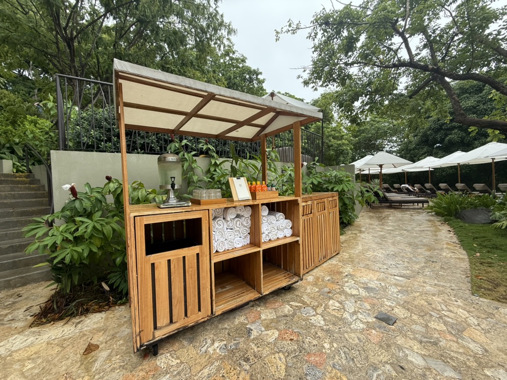 Small hut with towels, water, and sunscreen, with lounge chairs and umbrellas in the background.