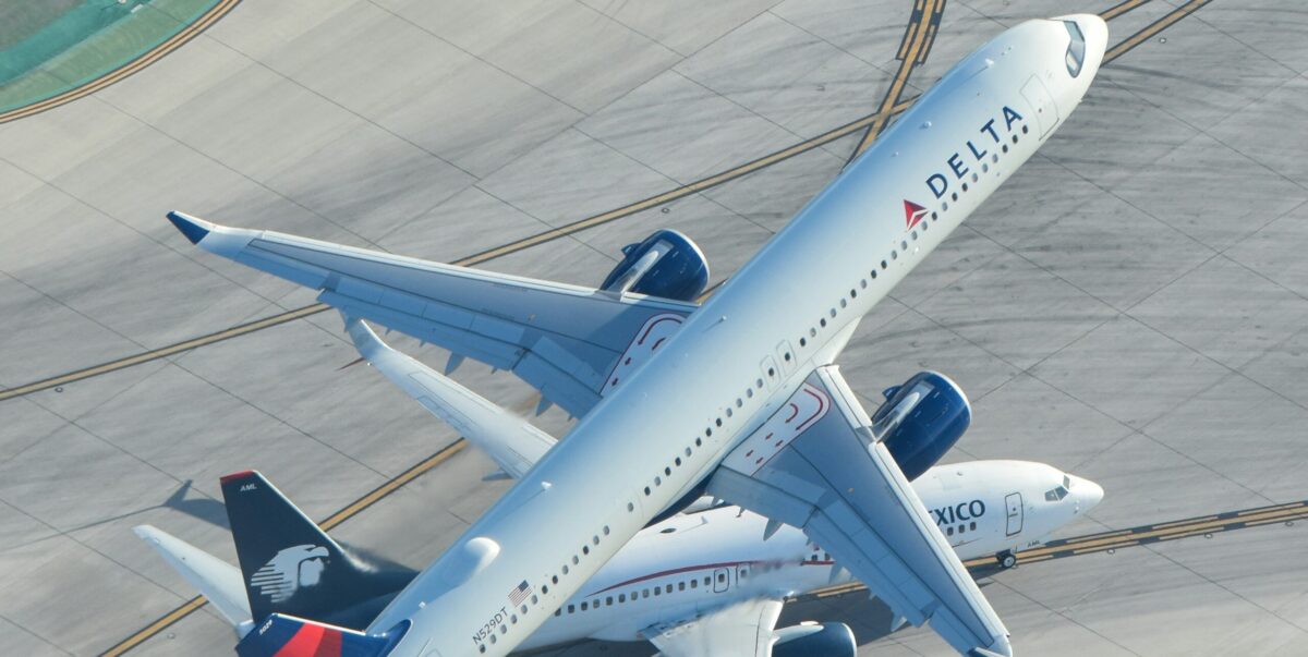 delta plane flying over an aeromexico jet on the tarmac