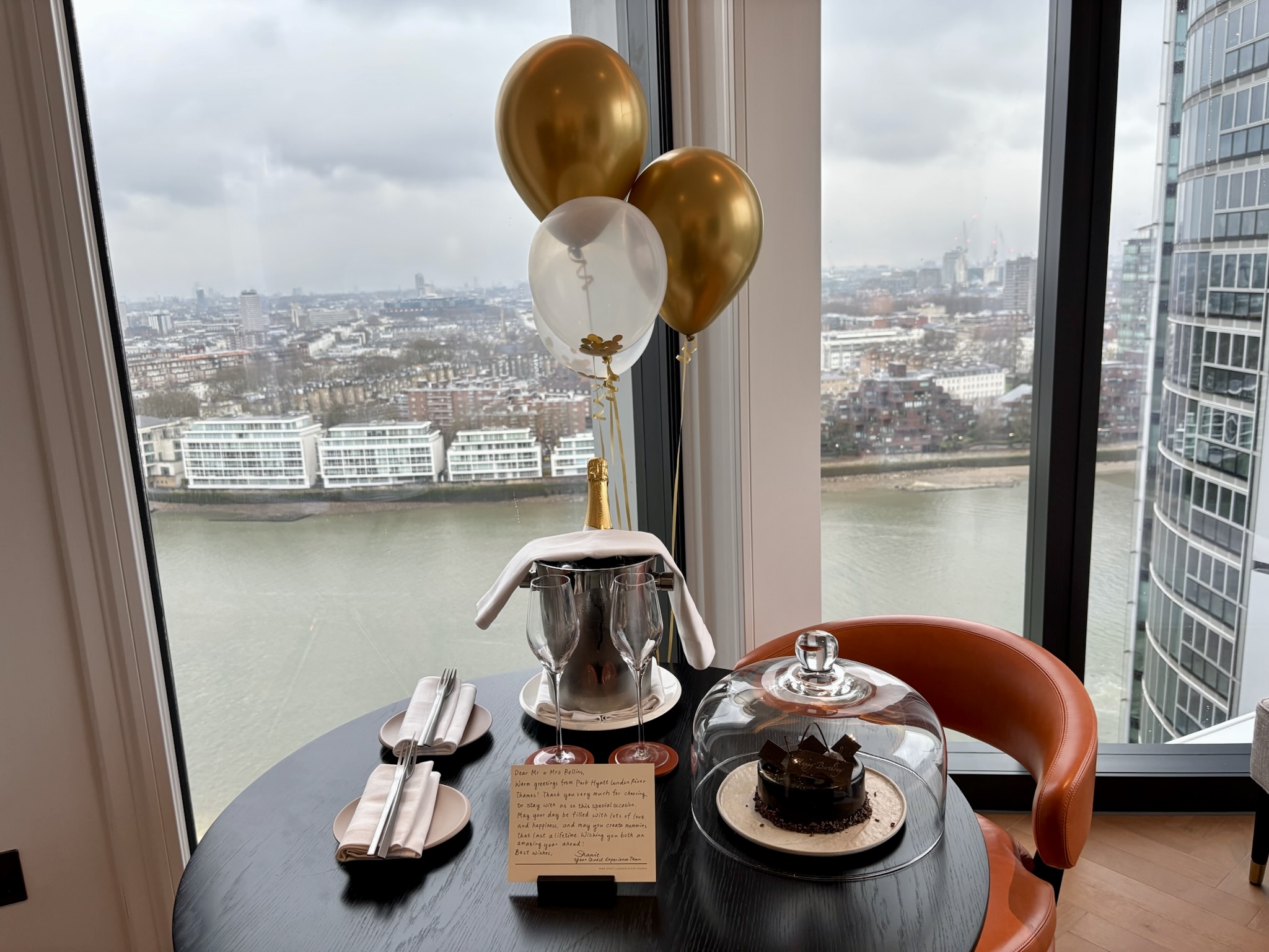 Inside the Park Hyatt London River Thames: Rooms, Dining, Pool & More 25 Balloons, champagne, and chocolate cake amenity on a table overlooking the Thames River