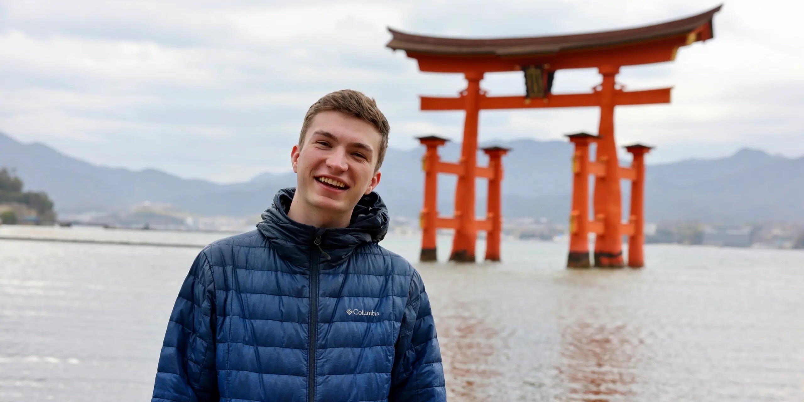 Thrifty Traveler's Kyle Thomas standing in front of an arch in Asia with a lake and mountains in the background