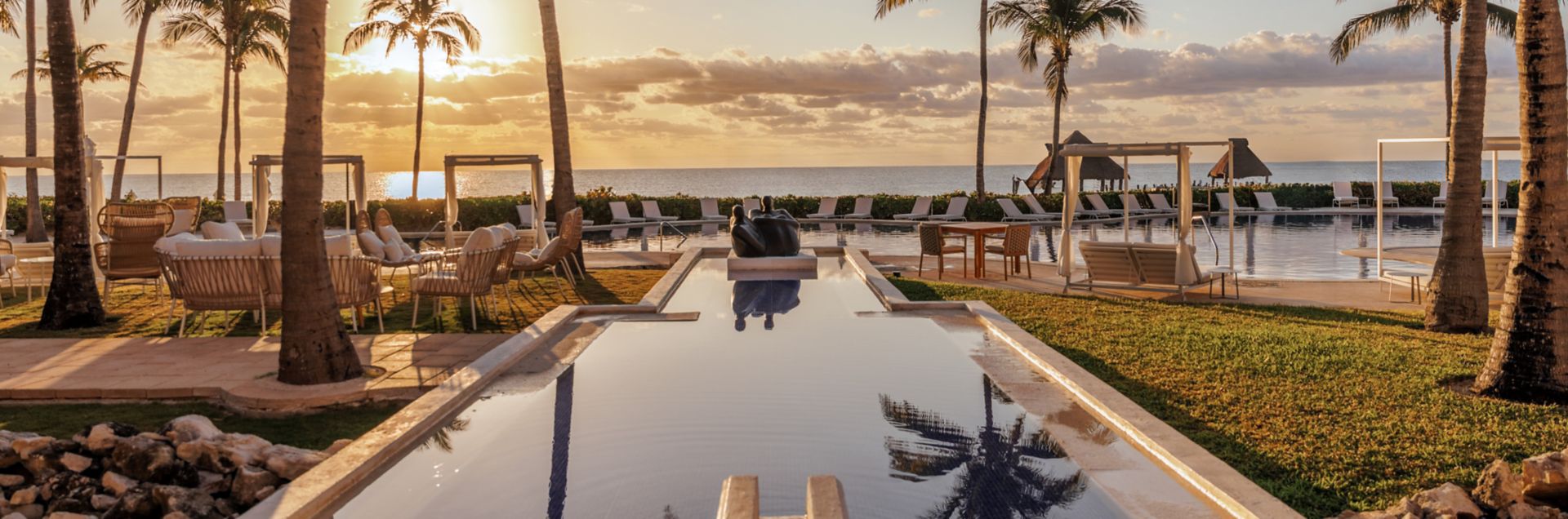 8 of the Best All-Inclusive Resorts in Cancún (Bookable With Points) 6 Reflection pool leading out to a beach with palm trees and sun setting over the water