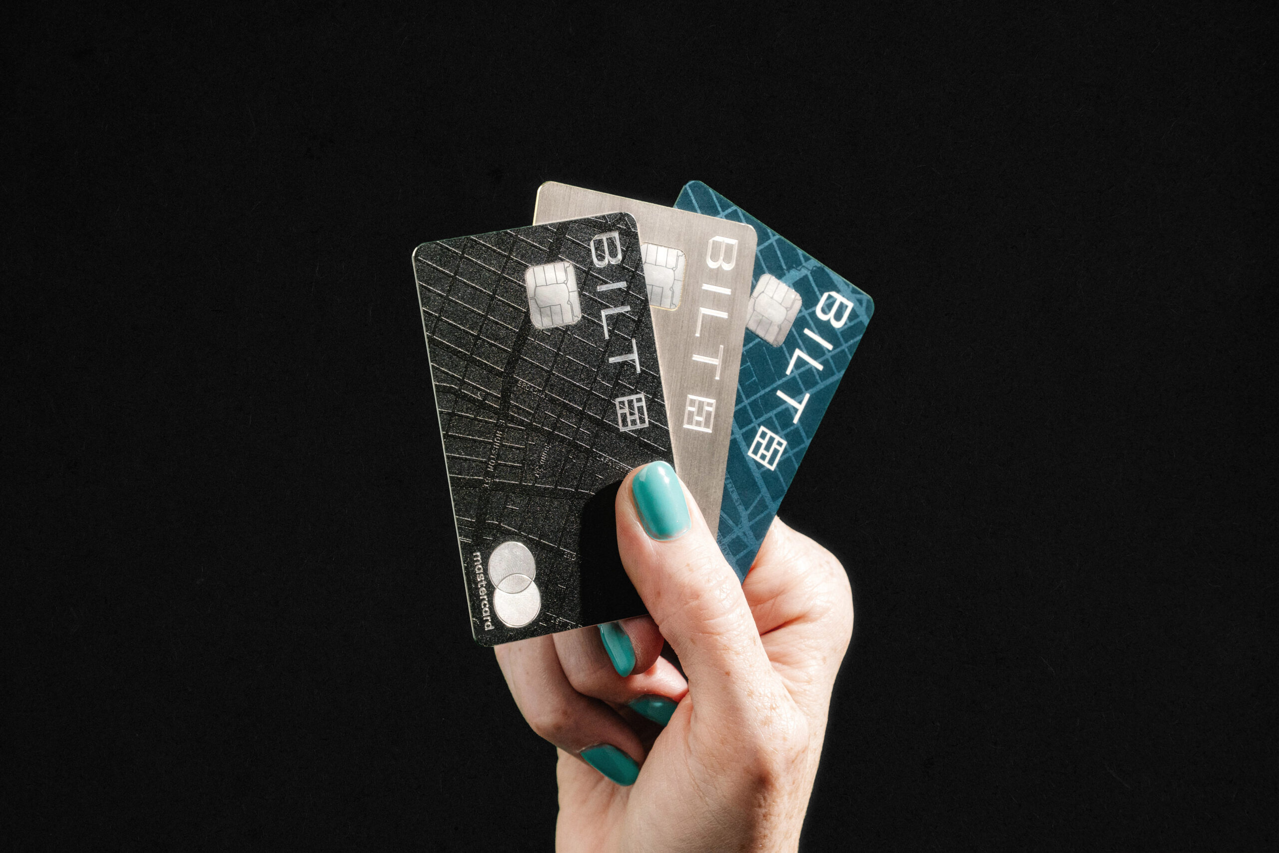 A hand holding the Bilt Obsidian, Palladium, and Blue Cards on a black background.