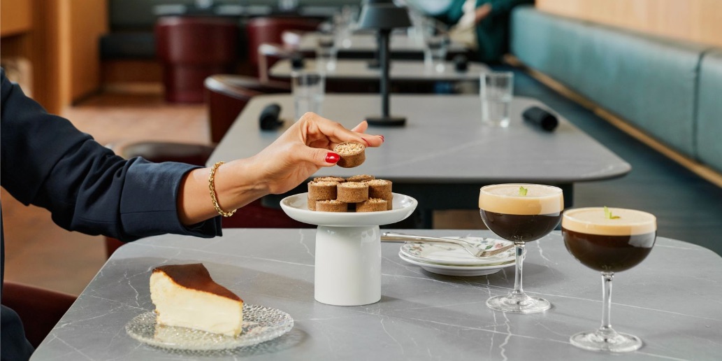 After a 3-Year Wait, Capital One’s 'Flagship' Landing Is Ready to Open at LGA 5 cheesecake and espresso martinis on a table with booth seating and chairs