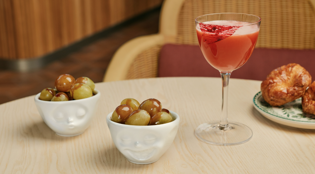 After a 3-Year Wait, Capital One’s 'Flagship' Landing Is Ready to Open at LGA 6 A drink, croissant, and bowls of olives on a table.