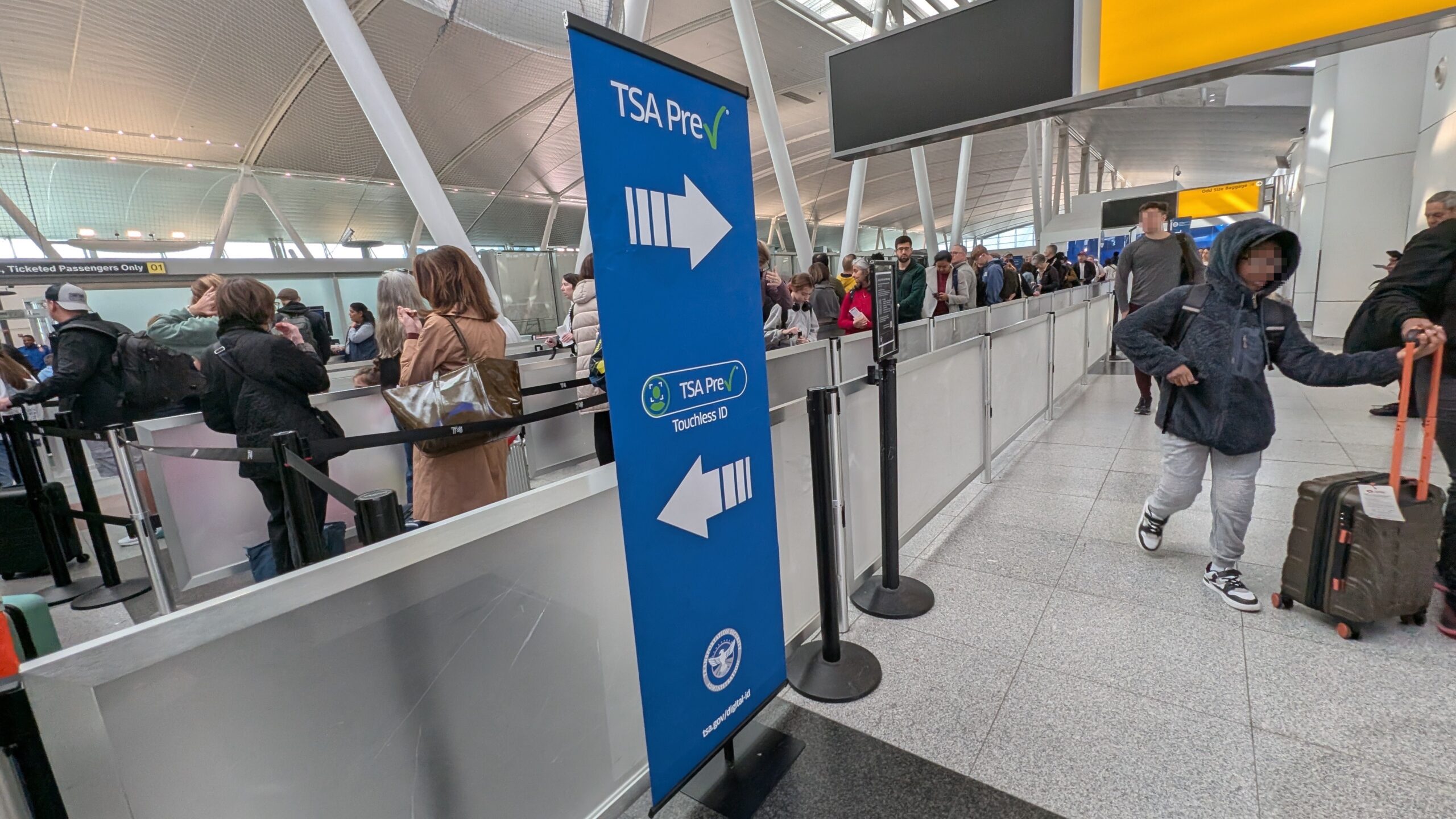 TSA PreCheck and TSA PreCheck Touchless ID sign at an airport with lines of people
