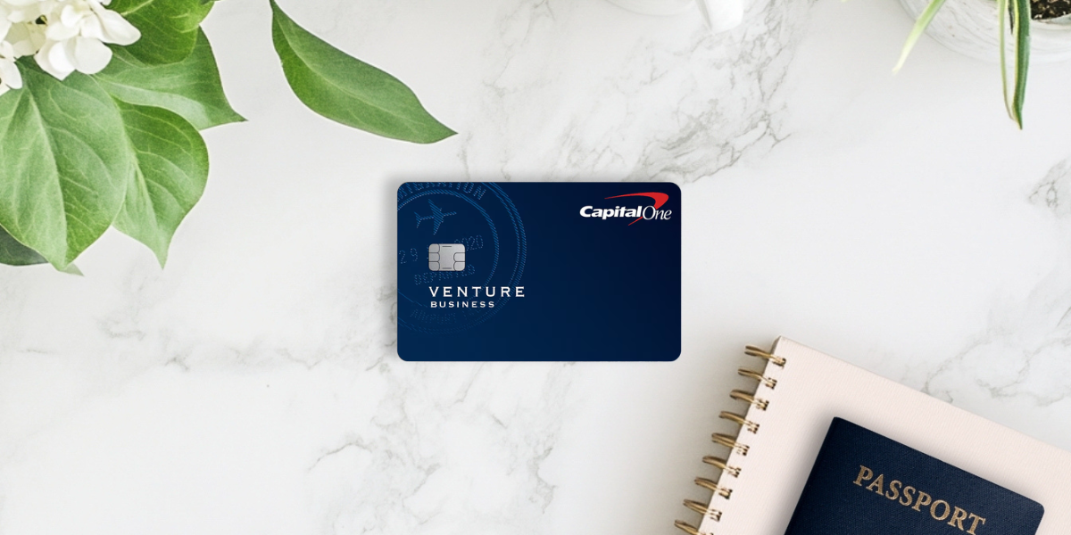 Capital One Venture Business card on a marble table with a notebook and a passport