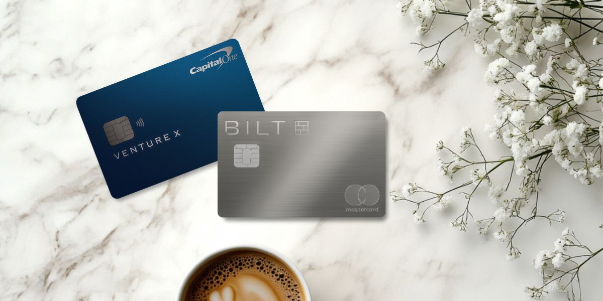 Venture X & Bilt Palladium cards on a marble countertop with floral arrangement and cup of coffee.