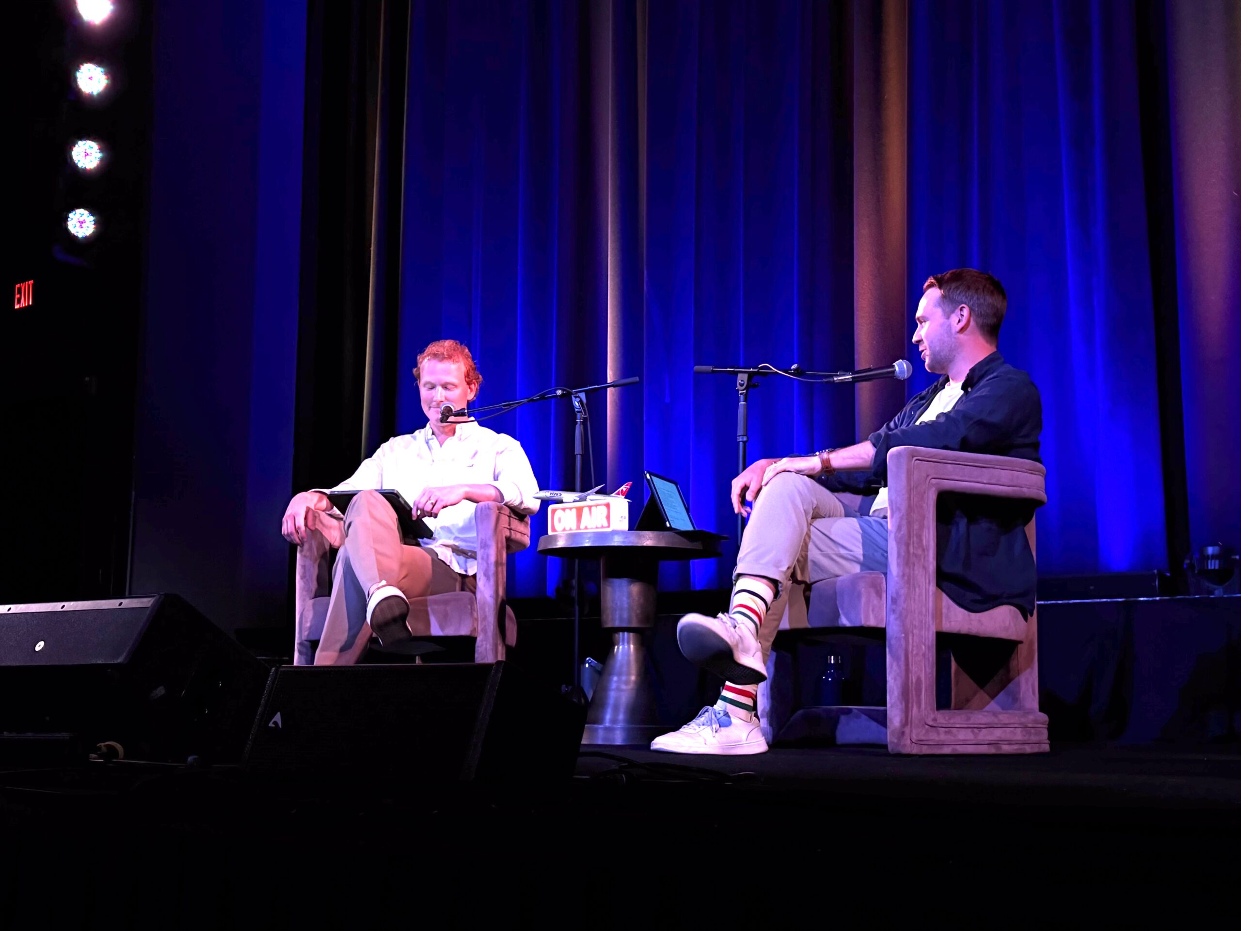 Recapping Our Live Podcast: Travelers Pack the Parkway for Hot Takes & Humiliation 3 two men speaking into microphones on a stage