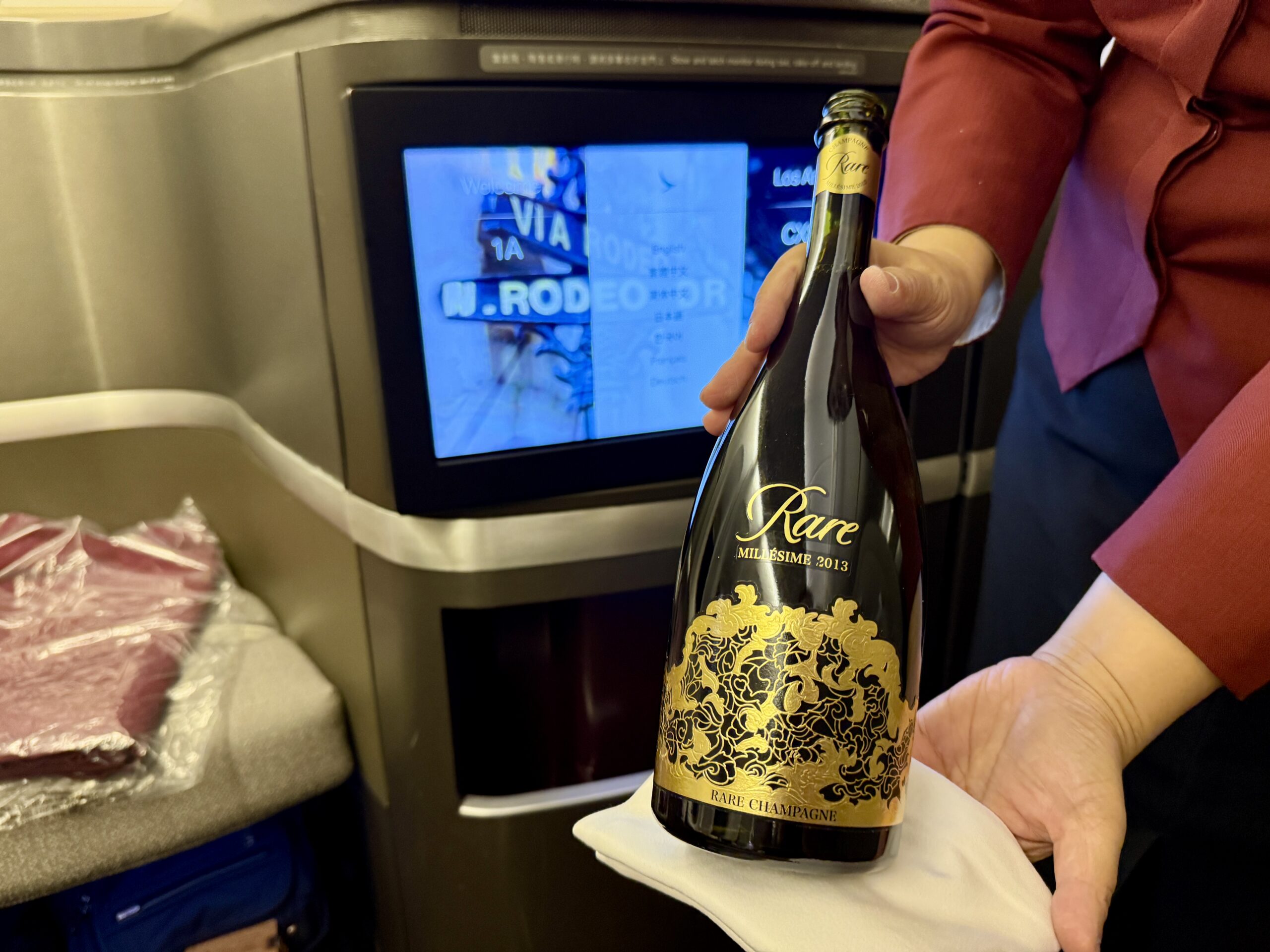 Aging Like a Fine Wine: Cathay Pacific First Class 777 Review 29 woman holding a bottle of rare champagne with a cloth underneath