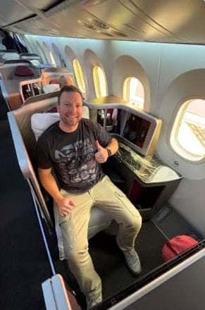 The Extra Mile, July 15: Pick Up the Phone to Book Business Class & More 2 Thrifty Traveler employee Jon Shalbetter in a business class seat giving the thumbs up