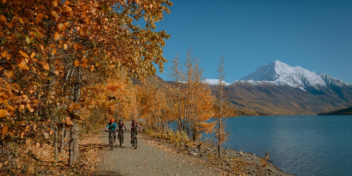 The Extra Mile, Oct. 5: Alaska Atmos Gets Even Better, Delta’s Great New Perk & More 2 people mountain biking on a trail, by a lake, with mountains in the distance.